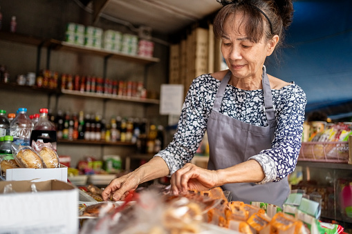 Active senior saleswoman working at a local grocery shop arranging products on market stall