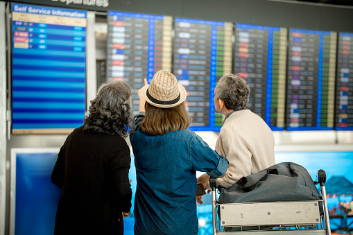 Group of travelers checking flight information at the flight information board. focus on a woman pointing at flight