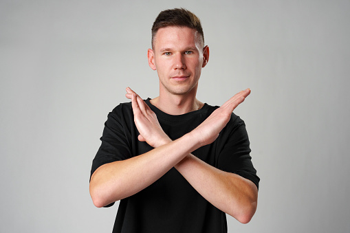 Young man showing x sign with crossed hands, meaning stop on gray background close up