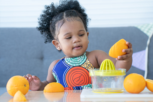 African cute kid girl squeezing fresh oranges at home. Adorable child happy to making freshly squeezed orange juice on manual juicer. Healthy lifestyle and learning concept