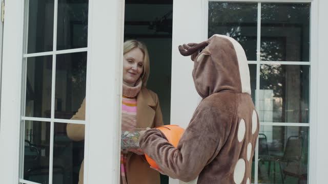 The child comes to get candy at the door of the house. Woman opens the door and gives a treat