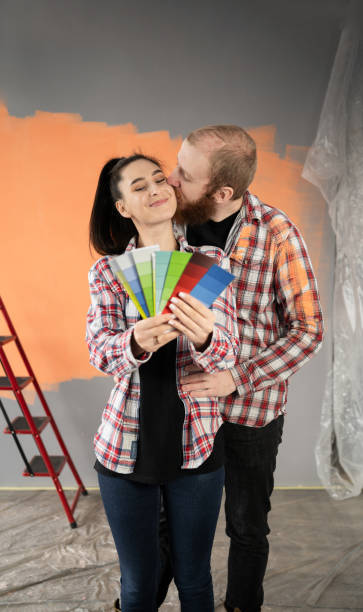 pareja de recién casados haciendo renovaciones en su nueva casa, eligiendo un color de pintura en una paleta, hombre besando a su esposa en la mejilla - home improvement couple painting real estate fotografías e imágenes de stock