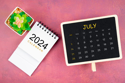 Calendar for July 2024 in black chalkboard on red wooden background.