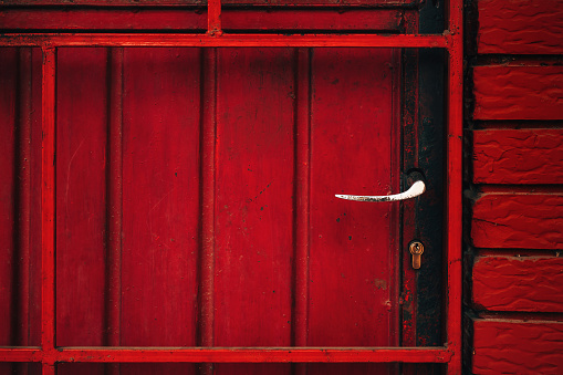 Old red metallic door with worn handle and lock