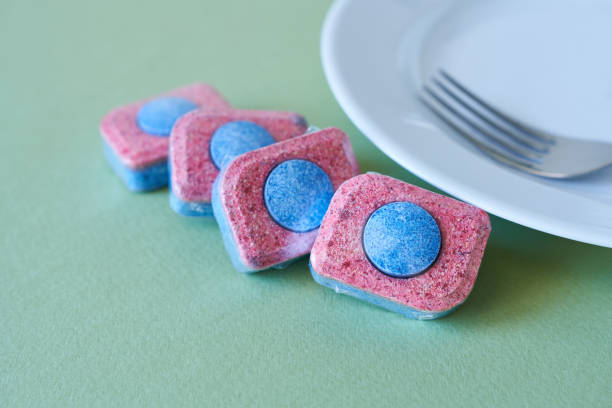istock Dishwasher tablets on a plate with a fork on a green background. 2103549062