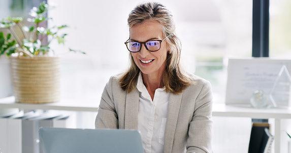 Mature woman, entrepreneur and smile with laptop to read in office for online, information and research for company. Boss, female person and ceo with vision for internet, e commerce and business idea