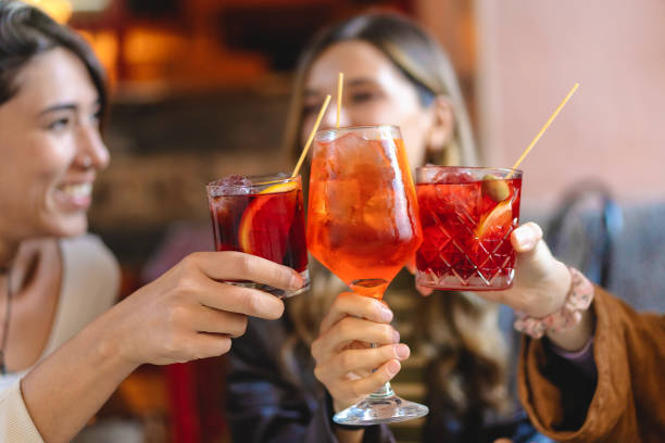 Female Friends Toasting Cocktails - Celebration and Refreshment Two joyful friends - toasting with vibrant cocktails - refreshing Spritz drinks, convivial bar atmosphere, moments of happiness and leisure - casual social outing, cheers to friendship, delightful aperitif time. alcohol drink stock pictures, royalty-free photos & images
