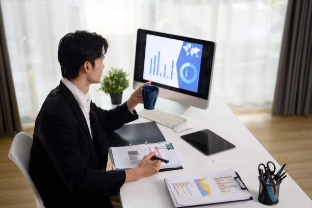 istock Focused businessman drinking coffee and analyzing sales data on computer monitor 2103573887