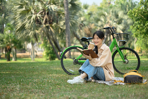 Happy young woman drinking coffee and reading book in the park.