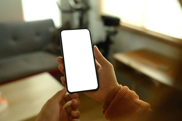istock Hands holding smartphone with empty screen standing in living room with warm light 2103574939