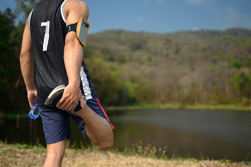 Male athlete stretching legs near lake before morning workout. Active lifestyle concept.