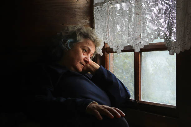 Side View Of Senior Woman Sitting By Christmas Tree On Table At Home