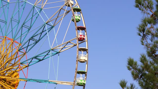 High carnival Ferris wheel in the amusement park in summer spinning against the blue sky