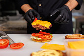 The cook in the kitchen prepares a cheeseburger and puts a cutlet with melted cheese.
