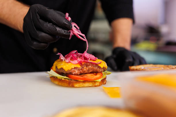 istock The cook in the kitchen is cooking a cheeseburger and putting onions. 2103609772