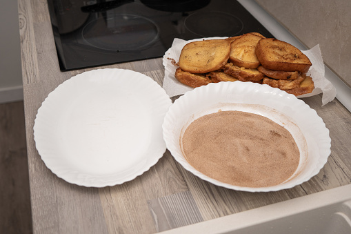 Fried torrijas browned on absorbent paper with a plate of sugar and cinnamon mixture, ready to be coated in batter.
