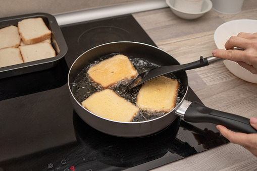 Hand using a spatula to flip soaking bread slices frying in oil for delicious torrijas.