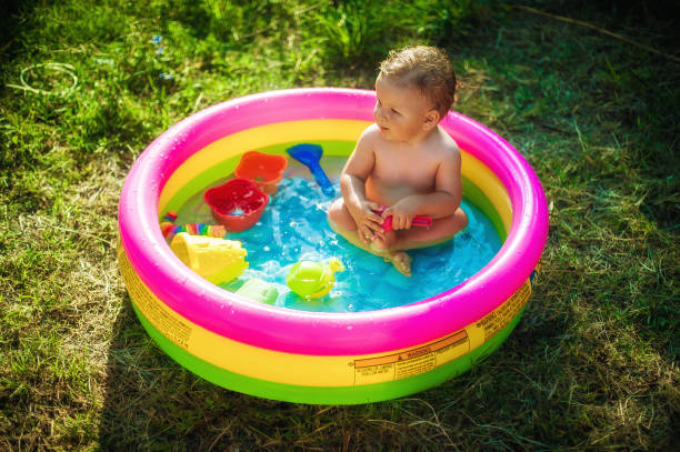 Baby is bathing in colorful wading pool on meadow field