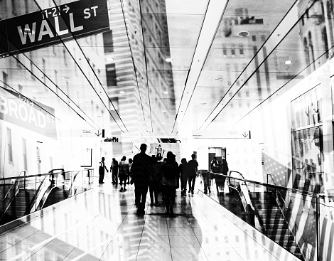 Shot of unrecognizable people walking on subway station superimposed over Wall Street cityscape, Lower Manhattan, NYC.