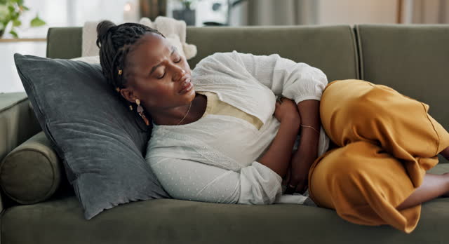 Woman, stomach and sick of pain on sofa for gut health, indigestion and gastric virus in lounge. African girl with ibs, menstruation and constipation of abdomen, endometriosis or bad bloating at home