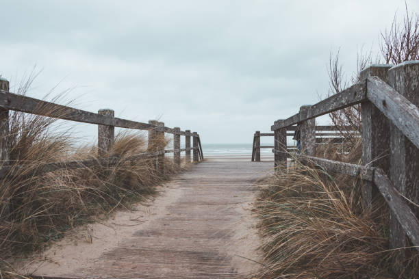 entrance to the sandy beach at blankenberge. a wooden pier under a heavy rainy sky - blankenberge strand stockfoto's en -beelden