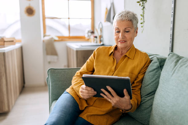 istock Senior woman shopping online by using digital tablet while sitting on a sofa at home 2103710655