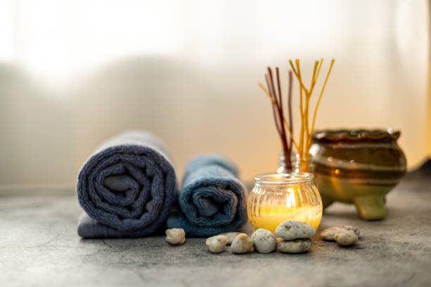 Image of Set of aromatherapy beauty spa essentials for rejuvenating wellness with scented candles, herbal scents, massage oils and roll towels on the stone table