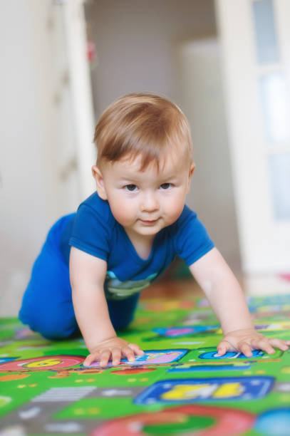 Baby boy crawls on the home floor and looking at camera. Front view. Kids innocence. Love and family emotion