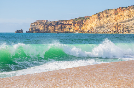 Wave and cliffs in Atlantic Ocean on the beach in Nazaré, Portugal.