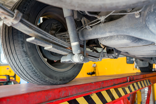 A car is on a lift showing its underside with a wheel, leaf spring  and suspension components visible.