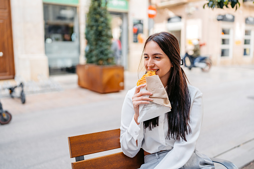 Beautiful young woman eating a pastry while sitting on a bench in Málaga in Spain.