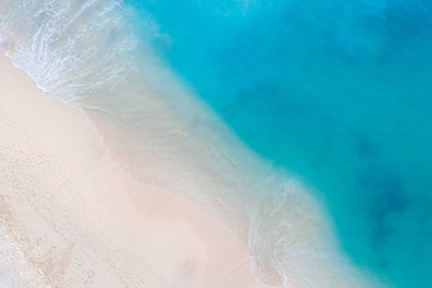 Aerial view of a serene beach with white sands meeting the crystal-clear blue waters. Gentle waves create intricate patterns on the shore. Bali.