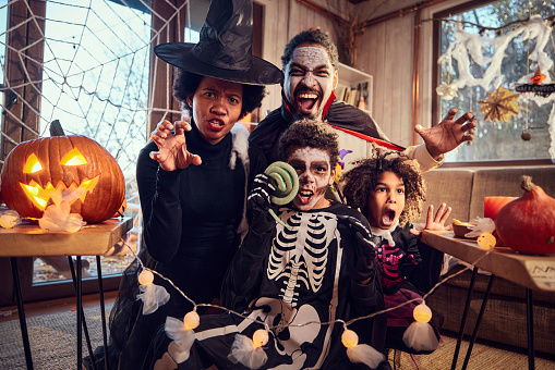 Spooky African American family in costumes having fun during a Halloween celebration at home and looking at camera.