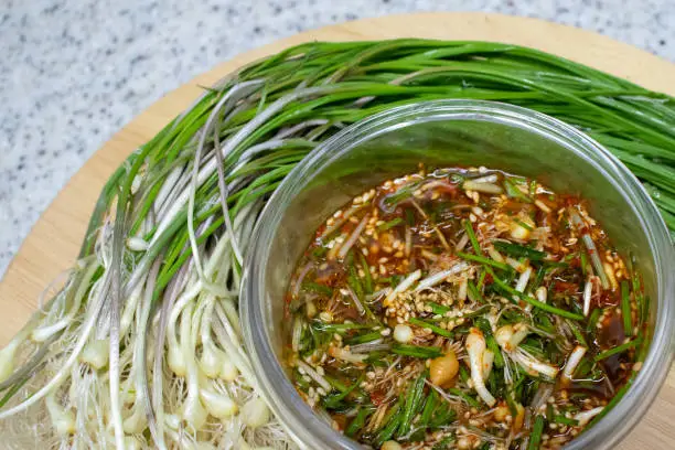 Dalrae seasoning sauce and fresh Wild Chive vegetables on a round wooden base. Dalrae seasoning sauce made with wild chives as the main ingredient, which Koreans enjoy eating in spring.