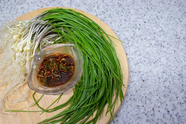 Fresh Wild Chive vegetables and seasoning sauce and on a round wooden tray. This seasoning sauce made with wild chives as the main ingredient, which Koreans enjoy eating in spring.
