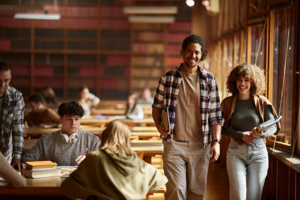 istock Happy college couple walking through full library. 2103842457