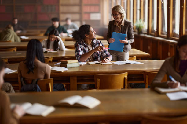 istock Happy senior professor talking to black student on a class in library. 2103849766