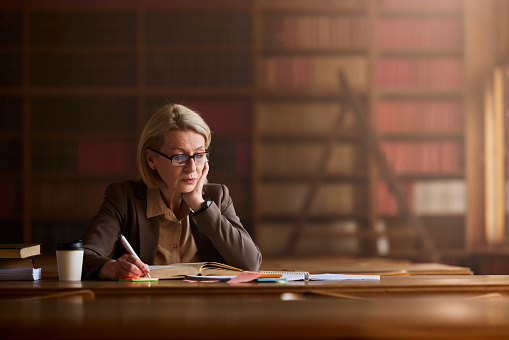 Senior female lawyer writing down her plans while reading a book in library.