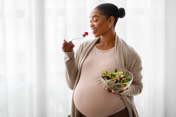 istock Happy Black Expecting Lady Eating Fresh Vegetable Salad At Home 2103864897