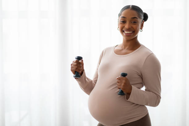 istock Cheerful athletic expecting black woman exercising with barbells 2103864905