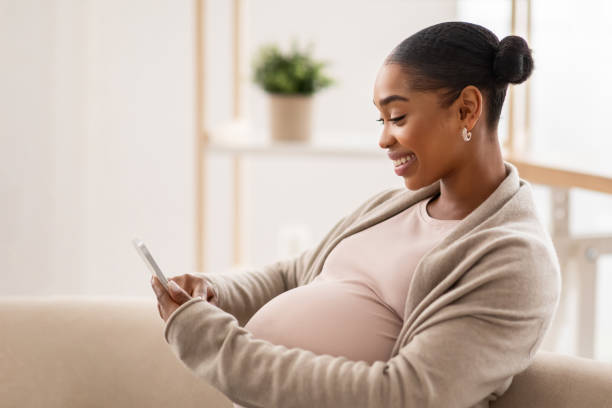 istock Beautiful african american expecting lady using cell phone at home 2103865486