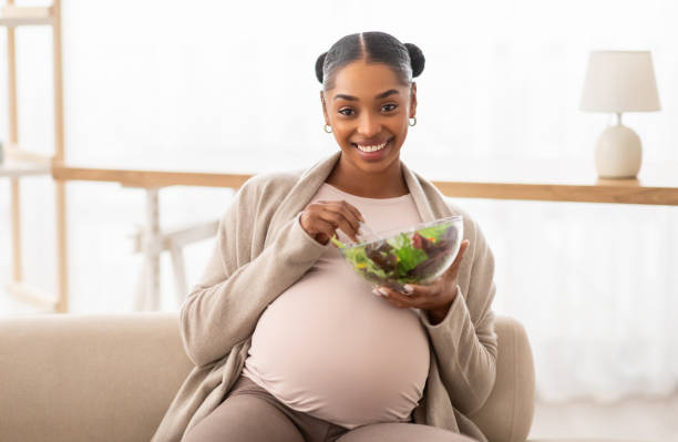 istock Happy young black lady expectant eating fresh vegetable salad 2103865493