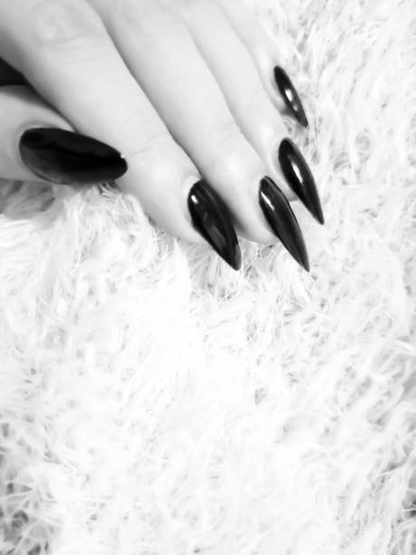 Woman hand with dark stiletto manicured nails on a light background with copy space, black and white edit
