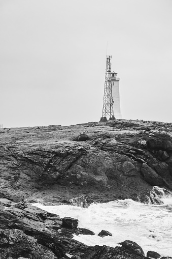 Dramatic Image of an icelandic Lighthouse with rough sea in the foreground. Captured in black and white. This lighthouse is part of an old NATO Base on the south coast of Iceland.