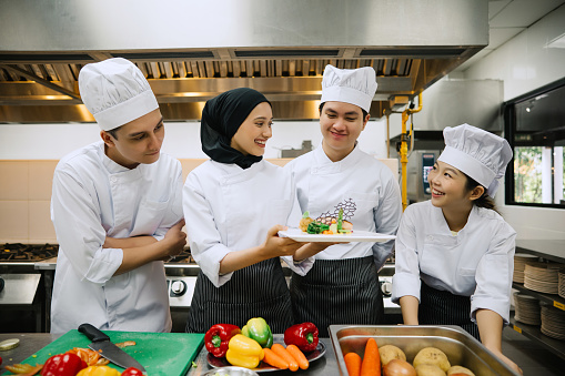Asian Female Chef Showing Her New Food To Her Colleagues In Kitchen.