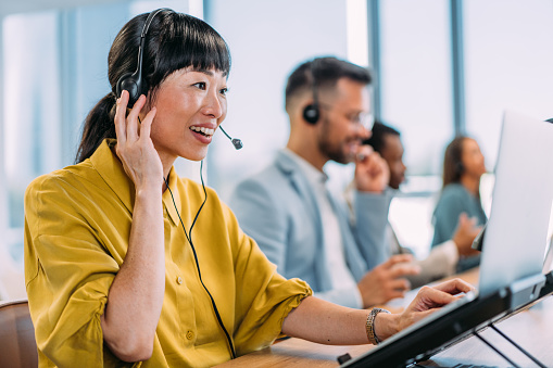 Shot of call center operators working in the office. Female call center agent working with her colleagues in modern office. Smiling beautiful businesswoman working in call center.