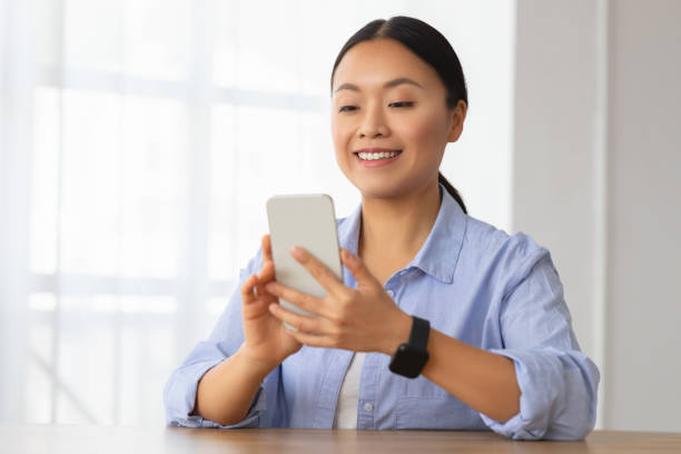 istock Cheerful asian woman using cell phone at home 2103896178