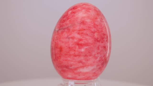 Red Marble egg rotating slowly on a turntable in front of a white background.