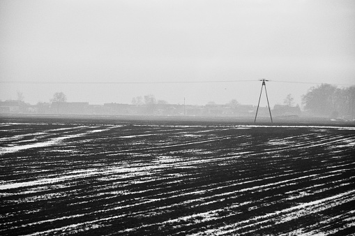 a vast, ploughed field with distinct furrows under an overcast sky, offering a view of a serene yet somber rural landscape