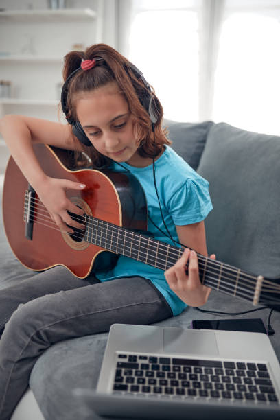 istock Kid playing guitar and watching video lessons on a laptop. 2103916570